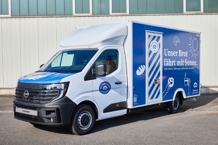 Blick von schräg vorne auf den parkenden Nissan Interstar-e mit blau-weißer Beklebung auf dem Bäckereikoffer und dem Schriftzug "Unser Brot fährt mit Sonne".