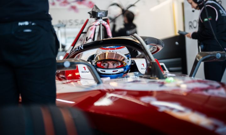 Oliver Rowland sat in the #1 car with his helmet on and visor up with team members around the car as he waits to go out on-track.