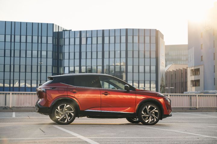Ein Nissan Qashqai in Fuji Sunset Red steht seitlich vor verglasten Hochhäusern