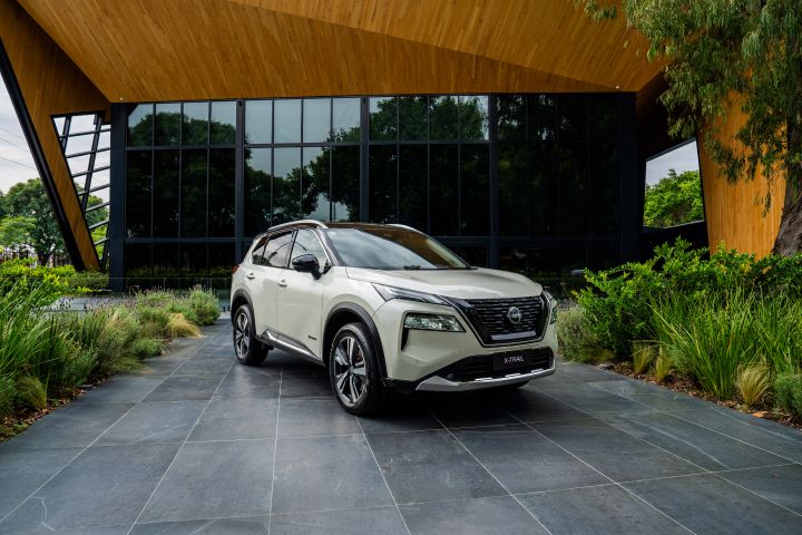 Nissan X‑Trail en color blanco. De fondo un marco de madera, plantas verdes y vidrios oscuros.