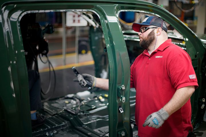 An image of a manufacturing team member with one arm reaching inside the body of a green vehicle