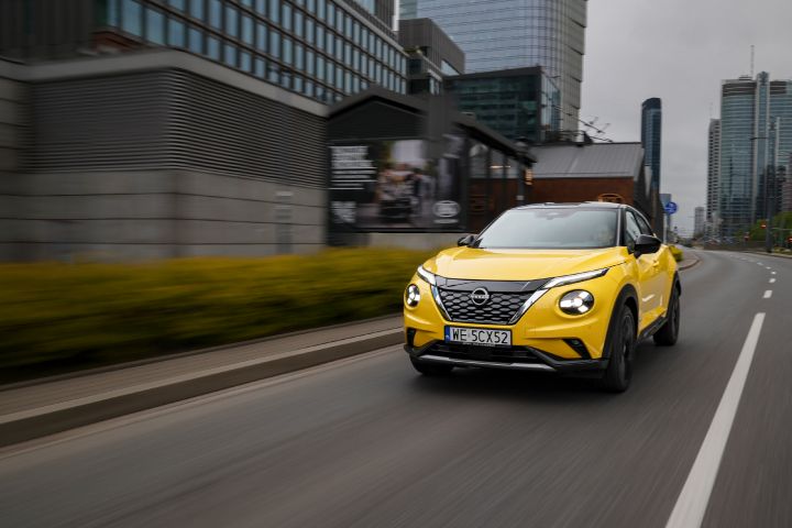 Jadący żółty Nissan Juke (widok z przodu) z budynkami w tle