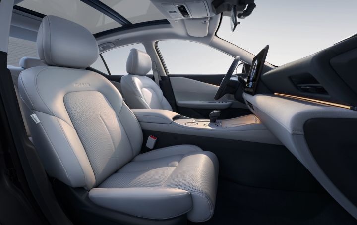 Close-up of the Teana’s interior front seats, featuring light gray leather upholstery. The center console includes a minimalist control panel and gear selector. A panoramic sunroof reveals the sky above.