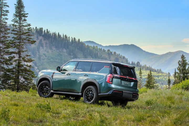 Left rear 3/4 view of a 2025 Nissan Armada parked on a grassy hilltop overlooking pine tree scattered mountains.