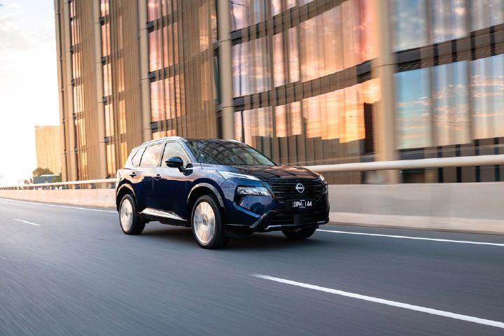 Dynamic front ¾ image of a 2026 Nissan MY26 X‑TRAIL SUV in Deep Everest Blue driving down a road