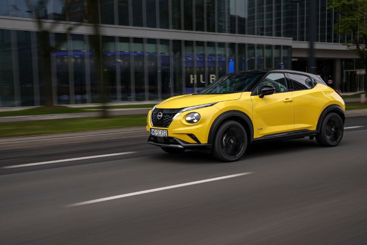 Jadący żółty Nissan Juke (widok z boku) z budynkiem w tle