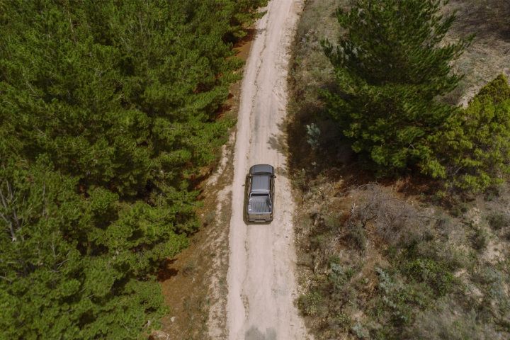 2026 Nissan Navara ST dual cab ute finished in Summit Silver viewed from above driving along a narrow dirt road through bushland.
