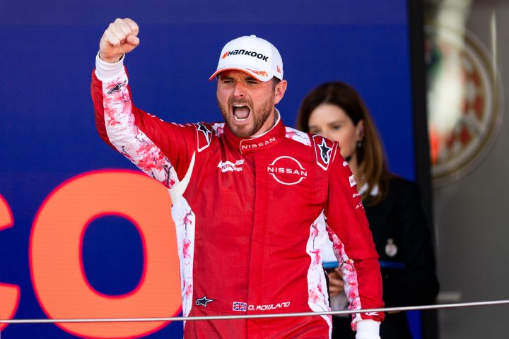 Oliver Rowland betritt in Monaco mit nach oben gereckter Siegerfaust in seinem roten Rennanzug des Nissan Formula E Teams das Podium.