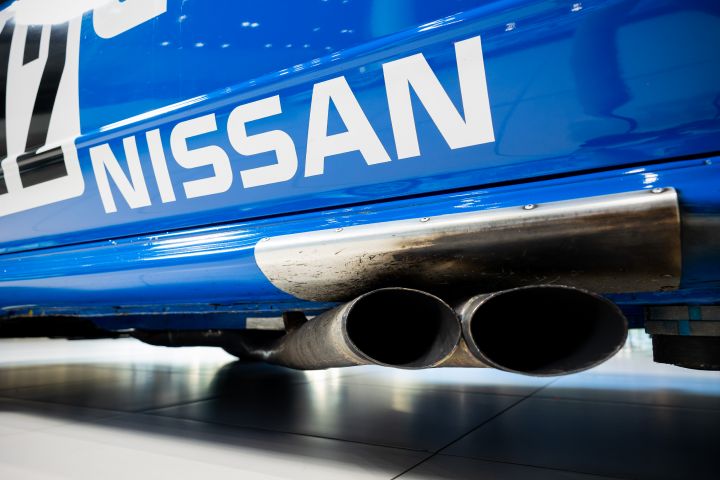 A close up image of the dual side exhaust on a blue GT‑R race car with text Nissan in white.
