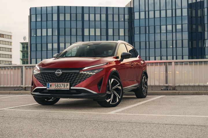 Ein Nissan Qashqai in Fuji Sunset Red parkt vor einem Hochhaus, 7/8 Front