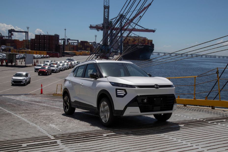 Nissan Kait branco sobe a rampa de um navio atracado no porto do Rio de Janeiro. Atrás dele, uma fila com outros Nissan Kait aguardam o embarque. Ao lado direito, é possível ver o mar