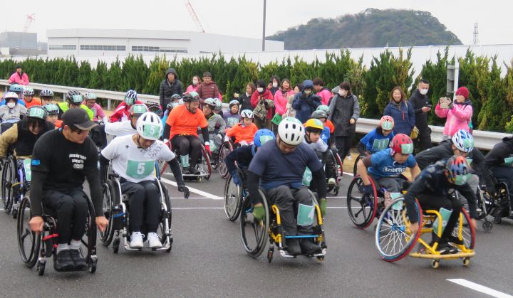 日産追浜工場内グランドライブを会場に、車椅子でマラソンのスタートを切る参加者と応援の人々