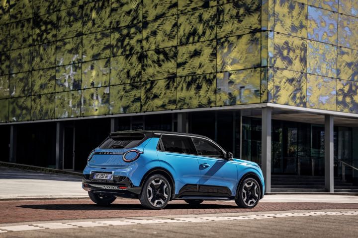 3/4 Heckansicht eines blauen Nissan Micra vor einem Gebäude mit grün bemalter Glasfassade