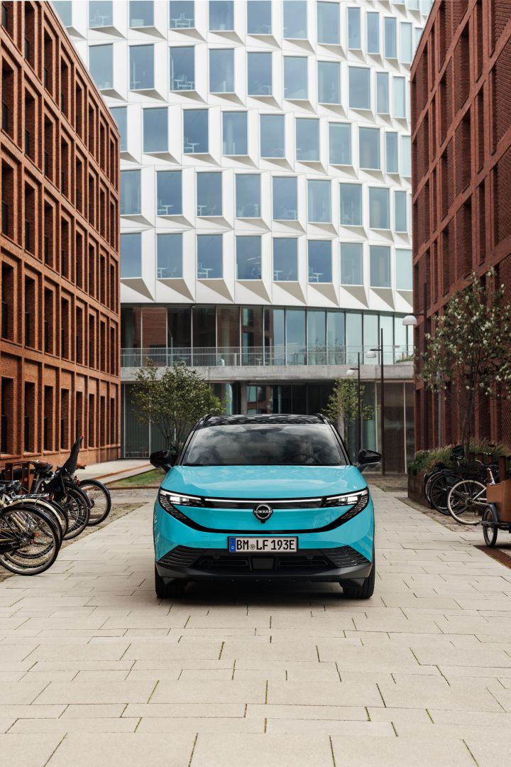 Hochformatige Frontalaufnahme eines türkisen Nissan LEAF, der zwischen modernen Hochhäusern steht