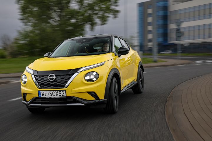 Jadący żółty Nissan Juke (widok z przodu) z budynkami w tle