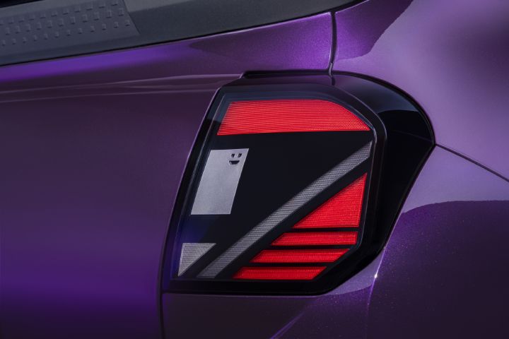 Photographie montrant un gros plan du feu arrière d’un véhicule violet avec des bandes LED rouges lumineuses, une bande rouge supérieure, des accents géométriques argentés et un motif de visage de robot.
