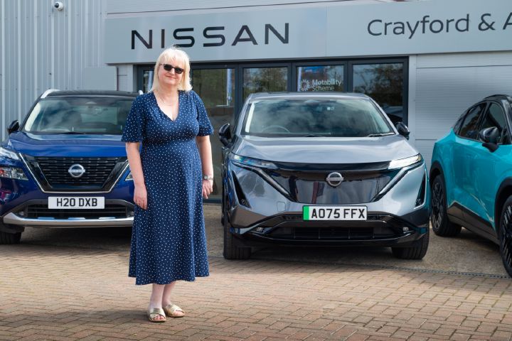 Person standing in front of a Nissan Ariya outside a Nissan dealership