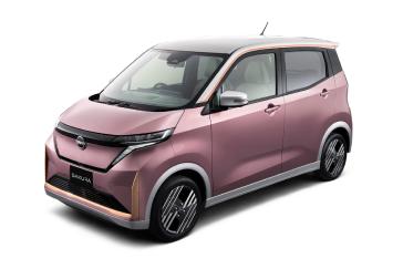 ピンク色の「日産サクラ」を、白いスタジオ背景の前で車両の左前方から斜め前向きに撮影した画像。やわらかなボディカラーとフロントデザインが際立っている。