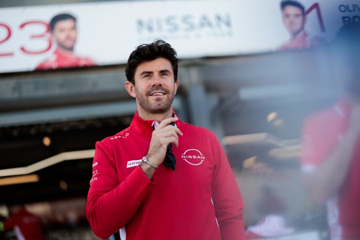 Norman Nato lächelt vor der Box des Nissan Formula E Teams, während er seinen roten Team-Pullover trägt.