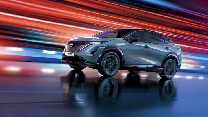 Dynamische 3/4 Frontansicht eines graublauer Nissan Ariya mit sportlichen, roten Designakzenten vor rotem Hintergrund