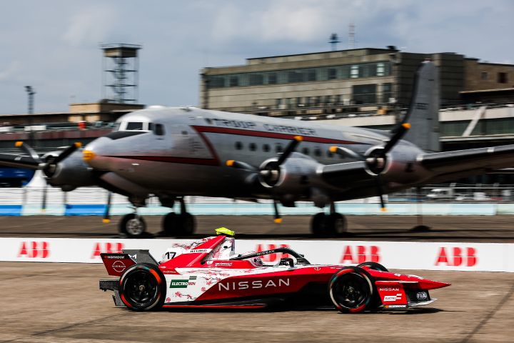 Carro de corrida da Equipe Nissan de Fórmula E no circuito do aeroporto de Berlim passando em frente a avião estacionado ao fundo