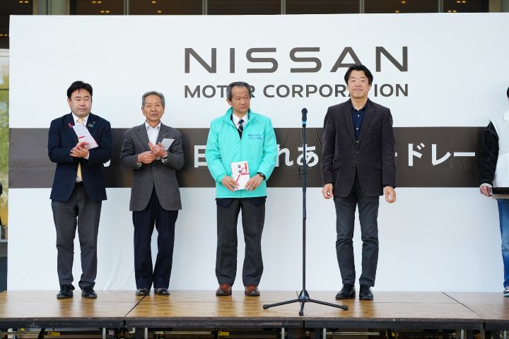 黒いジャケットを着た中畔EVPと3人の関係者が舞台上に並んでいる様子