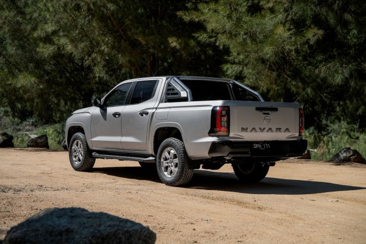 2026 Nissan Navara ST dual cab ute finished in Summit Silver shown from the rear-left three-quarter perspective, with the sports bar, tailgate embossing and black bumper.