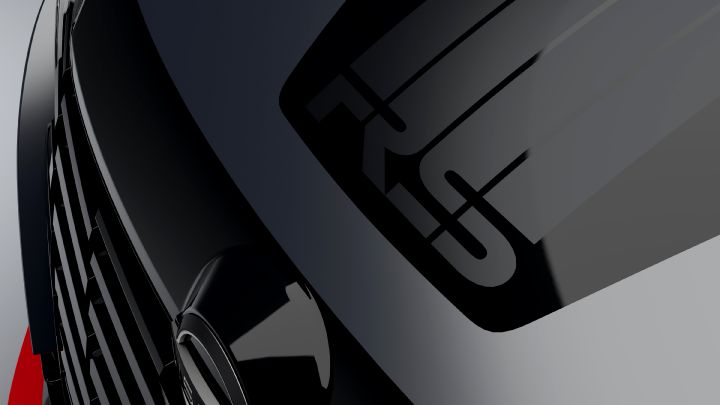 A close-up studio shot of the  hood of the Aura Nismo RS Concept, a silver and black two-tone sports car. The hood features black stripes. Part of the front grille and the Nissan logo are visible on the left side. The background is a simple gray, emphasizing the car's glossy finish and sleek details