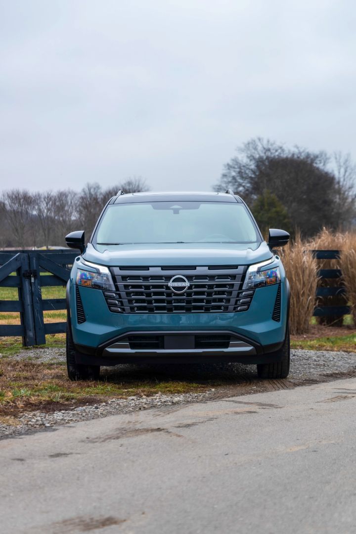 Front view of the 2026 Nissan Pathfinder parked in front of a gate with grasses nearby.