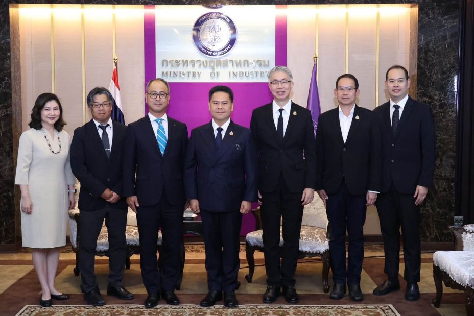 A group of eight people standing in a formal setting in front of national flags and an official backdrop, posing for a commemorative photo.