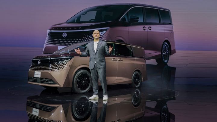 On stage, the all-new Elgrand is showcased, positioned diagonally facing slightly to the left. Next to the vehicle stands Nissan CEO Ivan Espinosa in a suit, delivering a presentation with both arms extended. In the background, a large screen shows a visual of the same vehicle.”