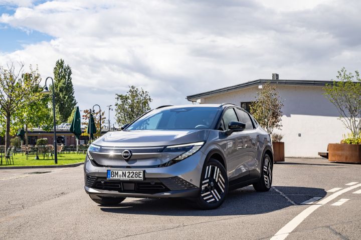 3/4 Frontansicht eines parkenden grauen Nissan Leaf, in dessen Motoraube die Sonne reflektiert