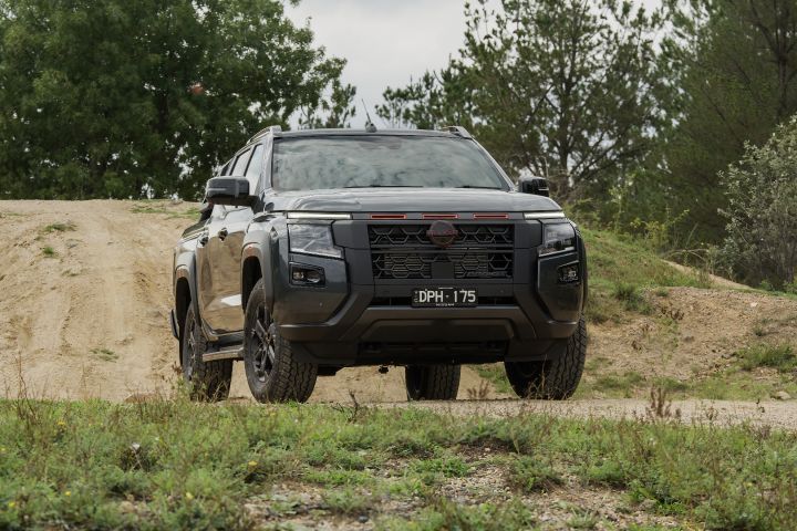 2026 Nissan Navara PRO-4X finished in Boulder Grey shown head-on atop a sandy mound with scrub, trees and a muted overcast sky in the background.