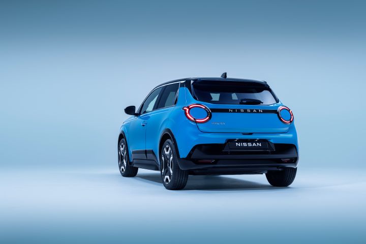 rear 3/4 view of Micra in blue gear color showing signature lit headlamps. Nissan name plate, driver & passenger doors, wheels, and black bumper