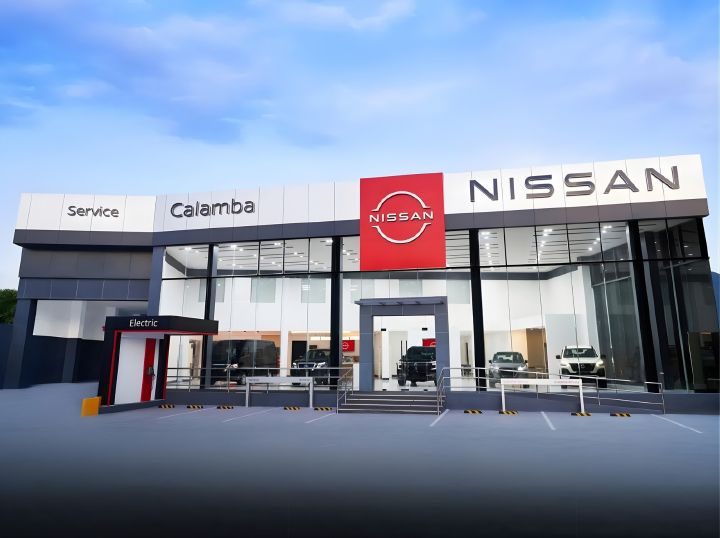 The modern exterior of the Nissan Calamba dealership featuring large glass windows, a service area, and an electric vehicle charging station.