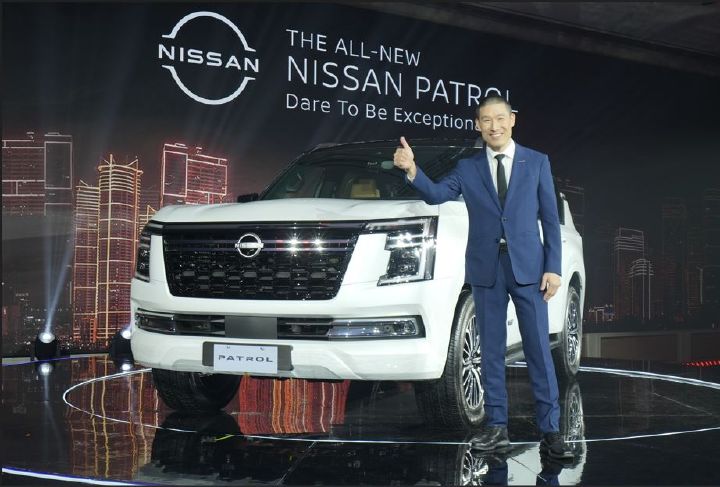 A photo of Ken Lee in a suit standing next to a white car