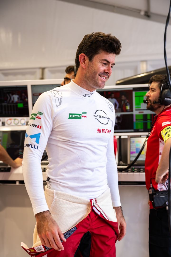 Porträtfoto von Norman Nato, der lächelnd in seinem weißen Untershirt in der Teamgarage steht.
