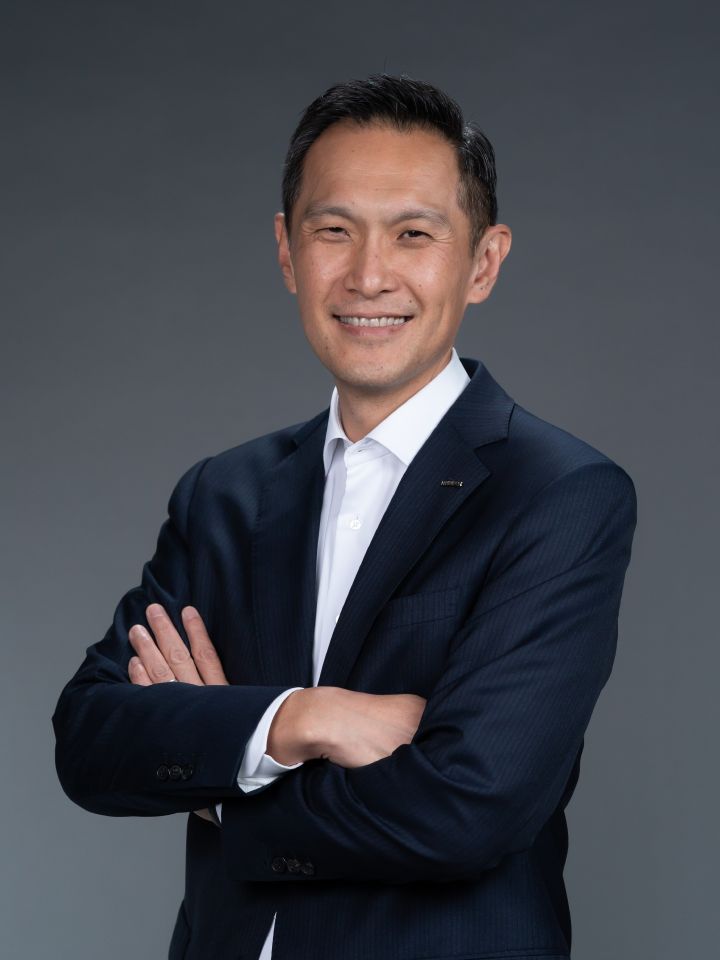 Portrait of Stephen Ma with his arms folded (suit, tie and NISSAN corporate pin) (smiling)