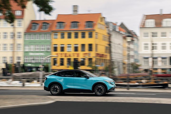 Seitliche Fahraufnahme eines türkisen Nissan LEAF vor bunten Stadthäusern in Kopenhagen, der Hintergrund ist verschwommen