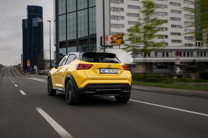 Jadący żółty Nissan Juke (widok z tyłu) z budynkami w tle