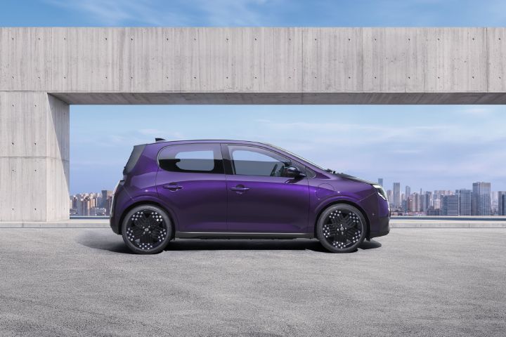Photograph showcasing a purple Nissan PIXO parked on a rooftop terrace. Side profile highlights aerodynamic shape, black alloy wheels concrete architectural frame, and city skyline backdrop.