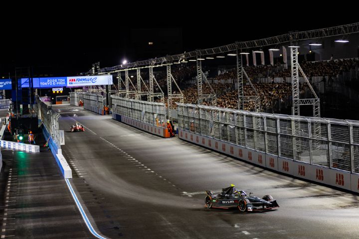 Aufnahme von Oliver Rowland im Auto mit der Startnummer 1, wie er beim E-Prix in Tokio in die erste Kurve einbiegt, während sich auf der nassen Strecke eine trockene Fahrspur abzeichnet.