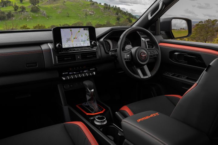 2026 Nissan Navara PRO-4X finished in Boulder Grey featuring the passenger-side cabin angle with touchscreen, gear selector and red-highlighted armrest.