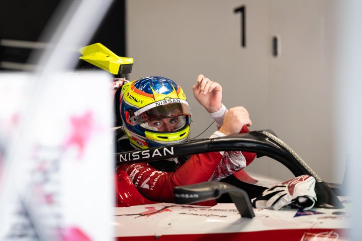 Eine Aufnahme aus größerer Entfernung, auf der Oliver Rowland mit seinem gelb-blauen Helm und hochgeklapptem Visier in der Teamgarage in das Auto mit der Startnummer 1 einsteigt.