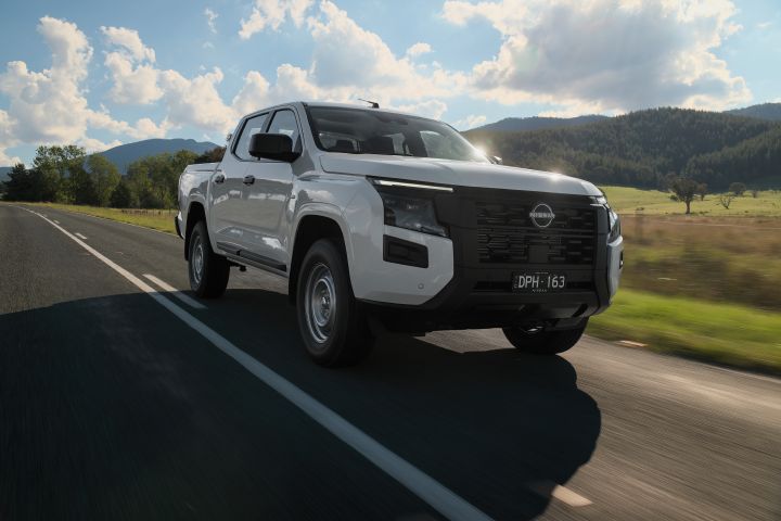 2026 Nissan Navara SL dual cab ute finished in Alpine White driving from a front-left perspective, showing the black grille, steel wheels and countryside surroundings.