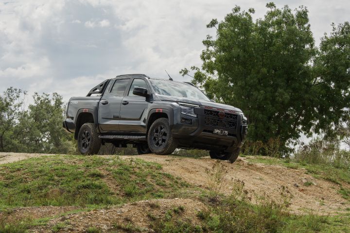 2026 Nissan Navara PRO-4X finished in Boulder Grey paused front three‑quarter on a mound highlighting clearance, black wheels and sports bar.