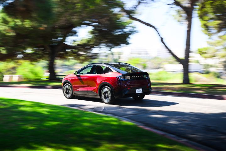 Angled rear view of the 2026 Nissan LEAF curving around a tree-lined drive.