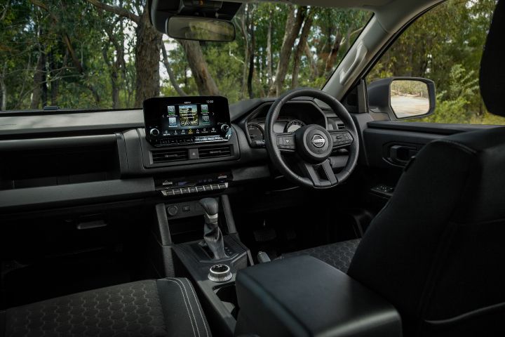 2026 Nissan Navara SL dual cab ute finished in Alpine White viewed from the rear of the cabin, showing the front dashboard, infotainment display, steering wheel and console layout.