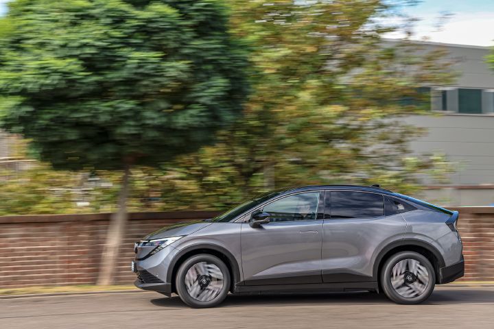 Seitenansicht eines grauen Nissan Leaf, der vor einer roten Backsteinmauer entlangfährt