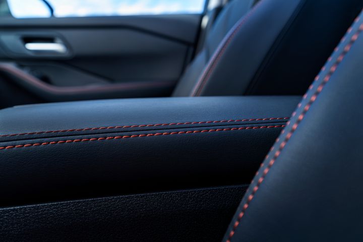 Der neue 2026 Nissan X‑Trail zeigt eine Nahaufnahme des schwarzen Lederinnenraums mit detaillierten magmaroten Nähten an Armlehne und Sitz. Der Fokus liegt auf der Handwerkskunst und den Designelementen, die den Kontrast zwischen glattem Leder und strukturierten Oberflächen betonen.